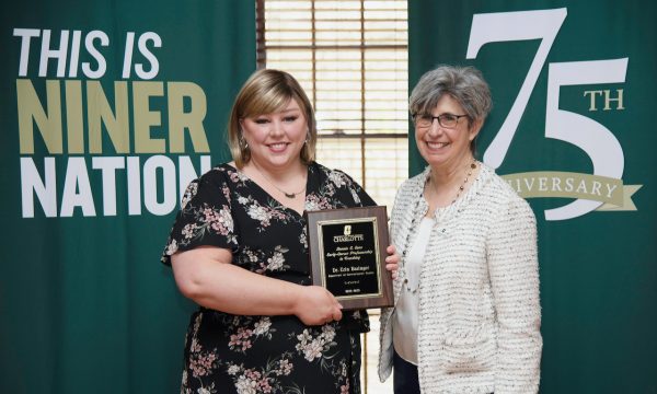 Erin Basinger and Joan Lorden in front of banners with the words This is Niner Nation and 75th anniversary