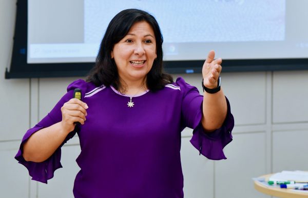 Susana Cisneros in purple dress gesturing as she teaches