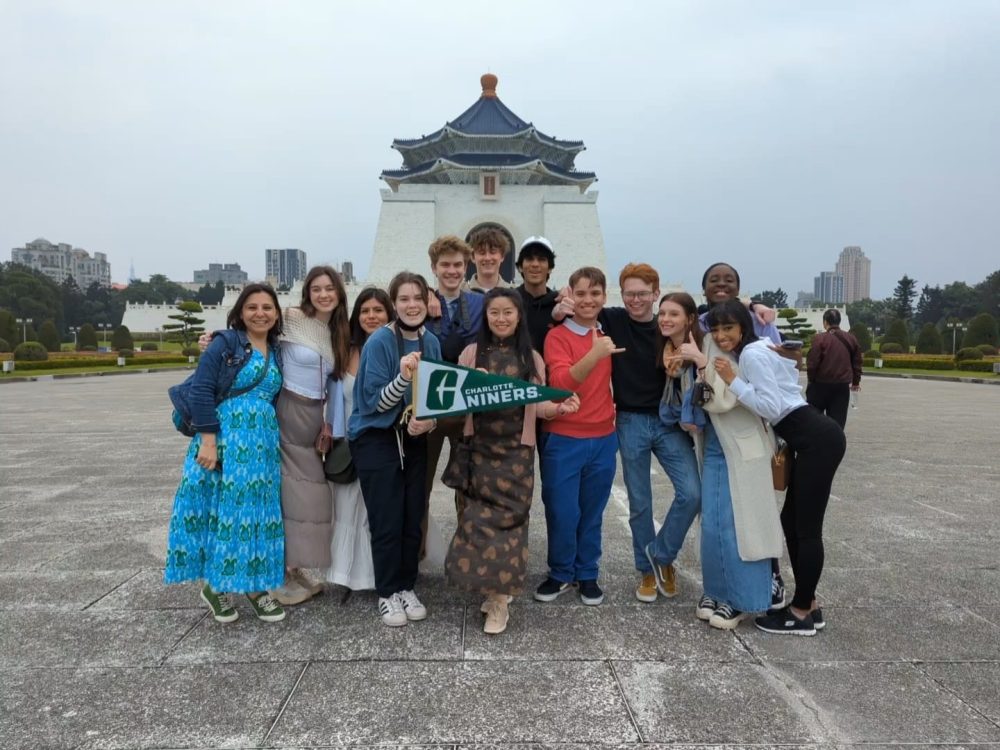 A Group of Charlotte students holding a UNC Charlotte pennant in Taipei, Taiwan with a