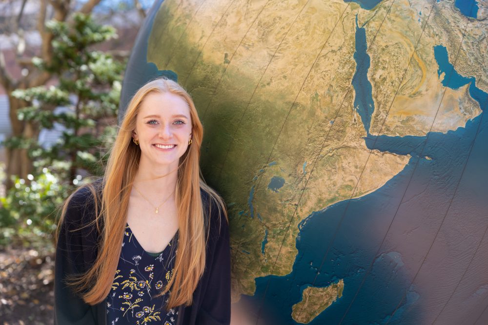 Mckenna zelna stands in front of the globe on campus.