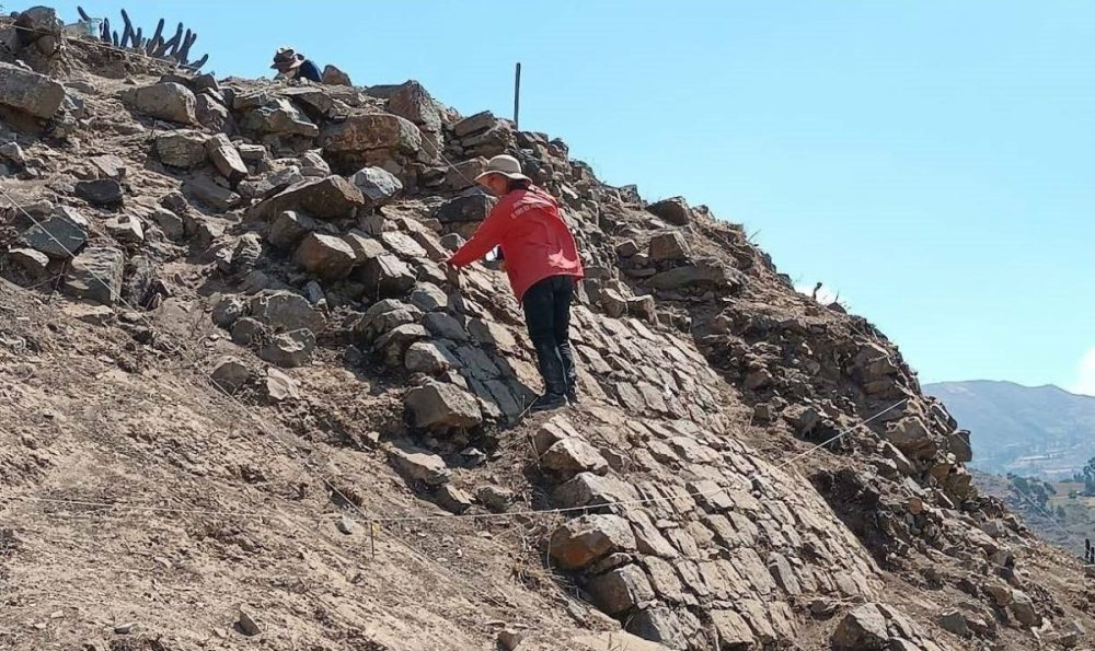 Amanda Brock Morales in the field, standing on the side of a steep hill in the desert, covered in stacked rocks.