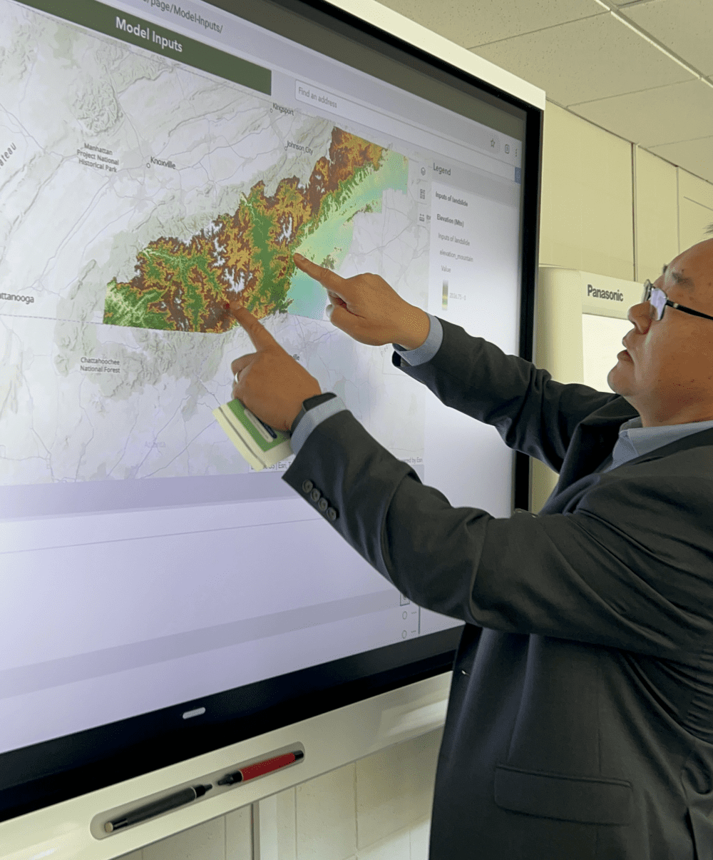 Tang is using two fingers to zoom in on a large screen to show a map of Western North Carolina's elevation reflected in different colors.