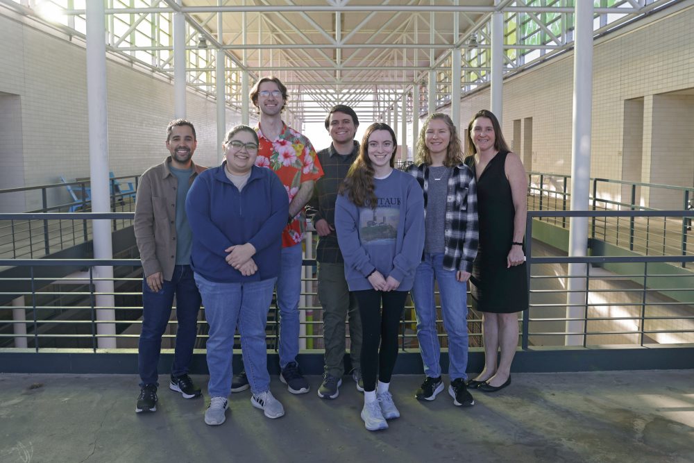 Six students and Amy Canevello stand outside on the balcony of the Colvard building at UNC Charlotte.