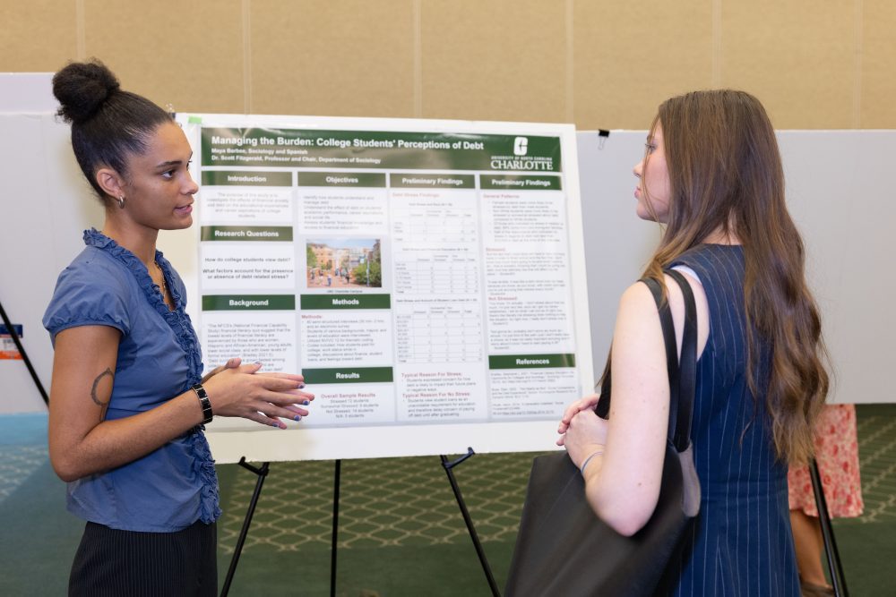 Maya Barbee stands in front of her research poster and talks with an attendee.