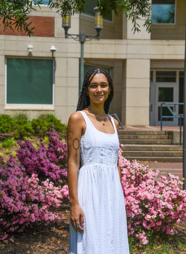 Maya Barbee stands near pink azaleas in front of the Fretwell Building at UNC Charlotte.
