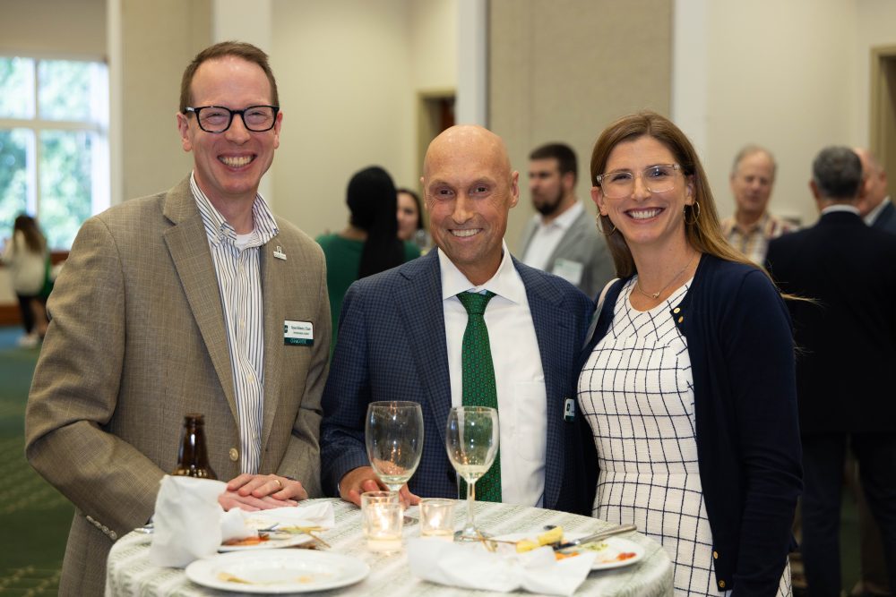 Ryan Kilmer, Dean Chris Boyer, and Erin Godly-Reynolds, pose at a standing table.