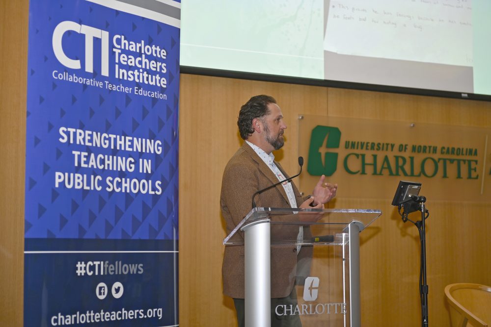 Scott Gartlan speaks to an audience next to the Charlotte Teachers Institute banner.