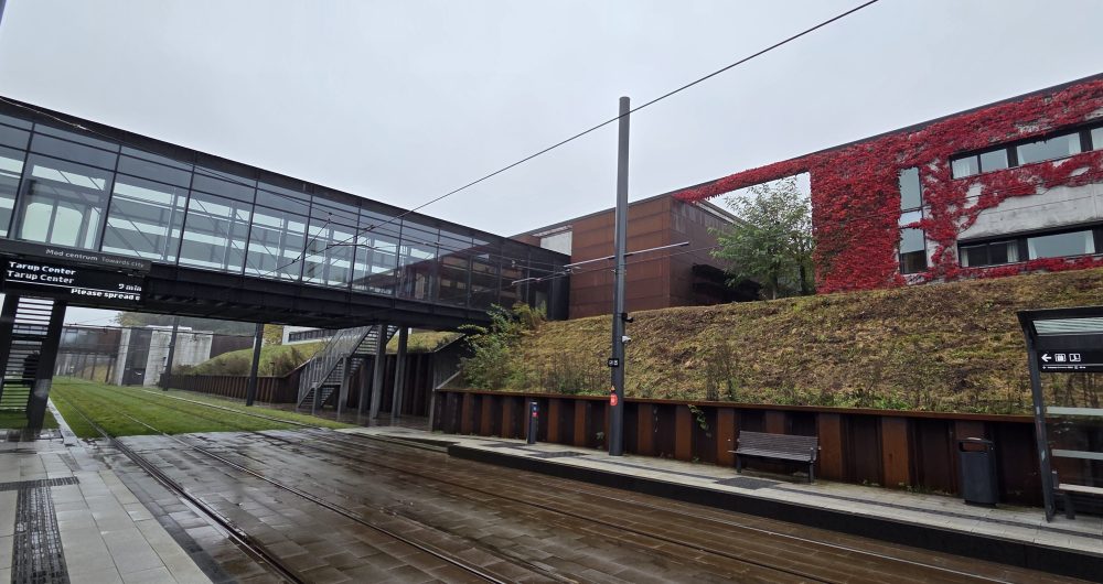 Train tracks with a red building and glass walkway in the background.