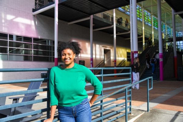 Madison Black wears Niner green and stands smiling against a raiking in front of Colvard on the UNC Charlotte campus.