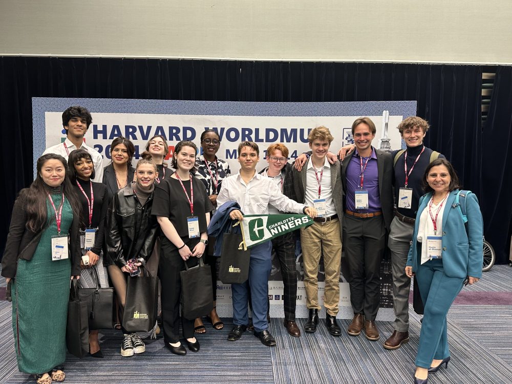 Al-Shamat and students posing for a group photo with a UNC Charlotte flag at the World Model United Nations in Taipei, Taiwan