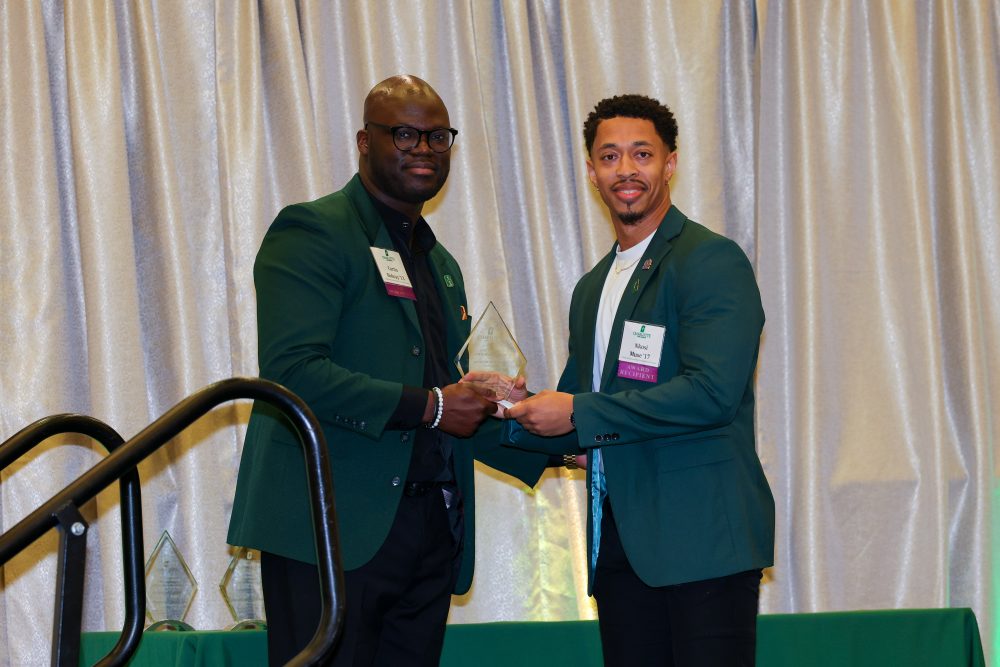 Two men on stage exchange the award and pose for the camera, smiling.
