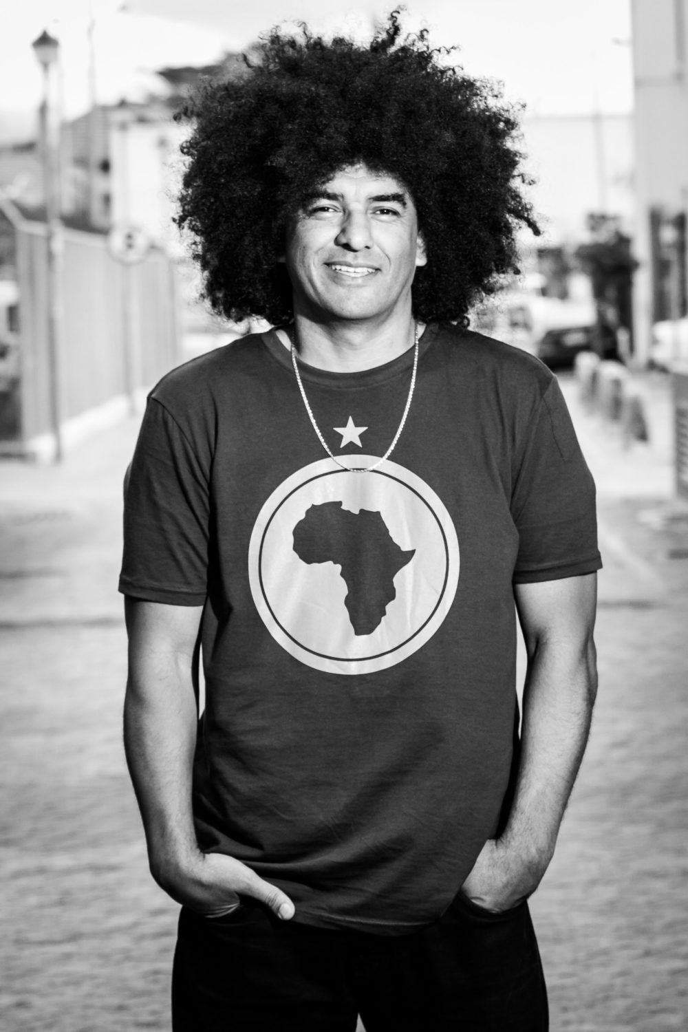 Man in tshirt with the shape of Afica on it stands smiling for the camera with his hands in his pockets.