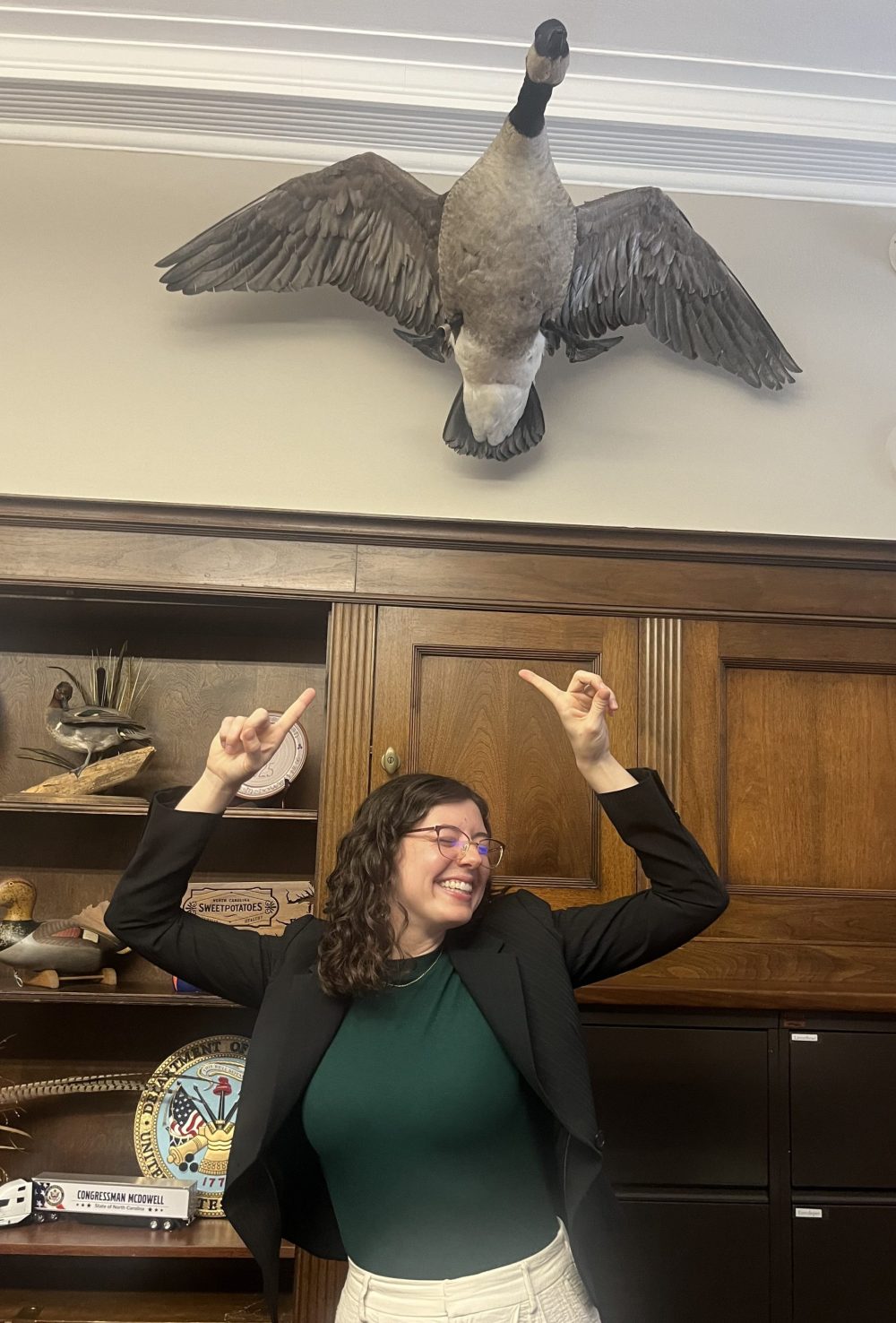 Elliott smiling and pointing up at a goose on an office wall.
