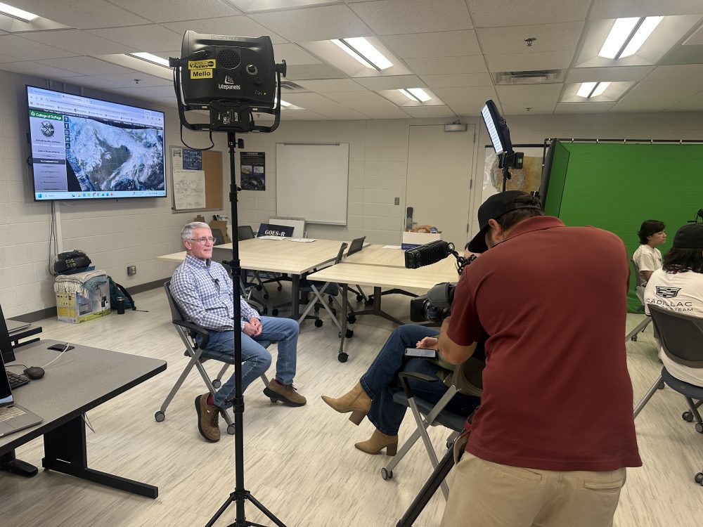 Steve Udelson sitting in a chair and getting interviewed for WSOC-TV with a cameraman in the foreground.