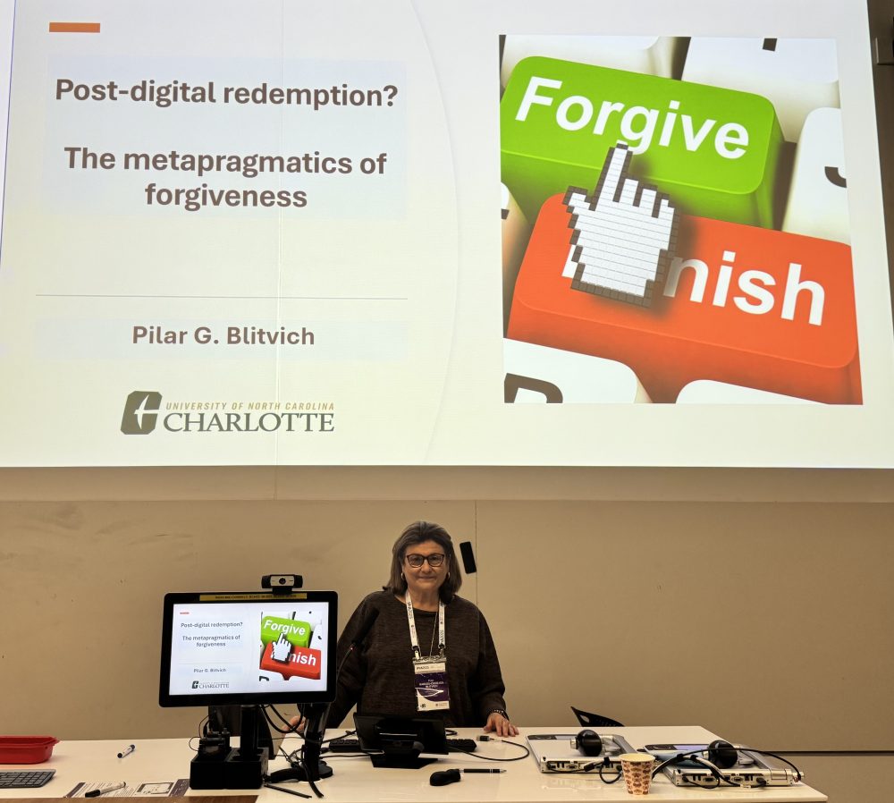 Blitvich in front of a large PowerPoint that is titled "Post-digital redemption? The metapragmatics of forgiveness"