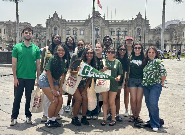 The group of World Model UN students and their advisor are dressed in green UNC Charlotte gear and holding a Go Niners pennant in Lima, Peru.