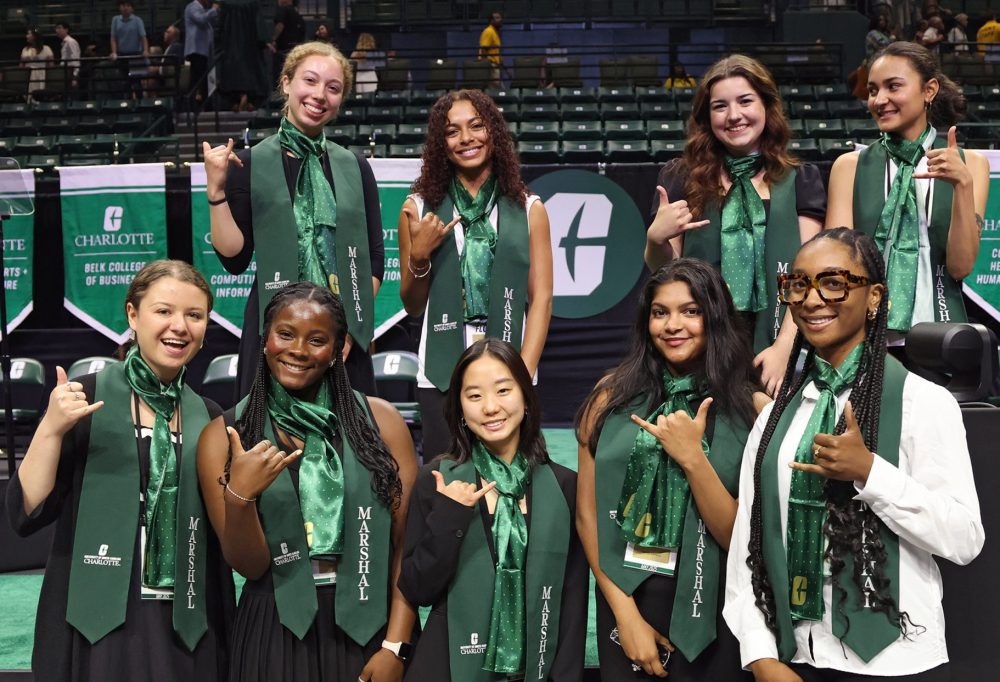 Frink and eight other student marshals pose in green in front of the stage after spring 2025 graduation.