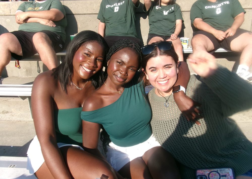 Frink and two friends in the stands at a UNC Charlotte football game.