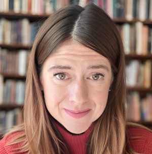 Helen Davies headshot in front of bookshelves wearing a red sweater