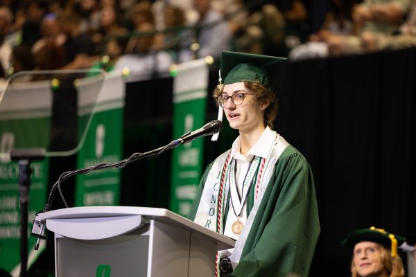 Foster Duckworth wears UNC Charlotte graduation regalia with stoles and cords and speaks at the podium during the commencement ceremony on Friday, May 8 at 3 p.m.