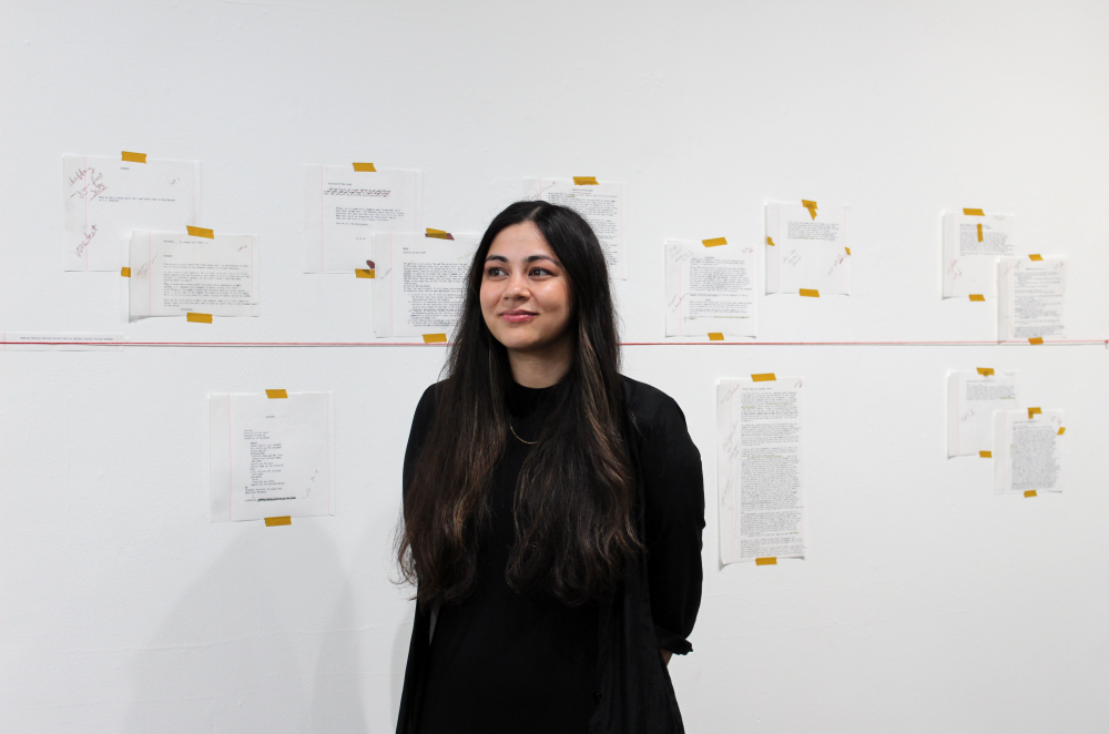 Hussey smiles in front of the gallery wall showcasing her first drafts.