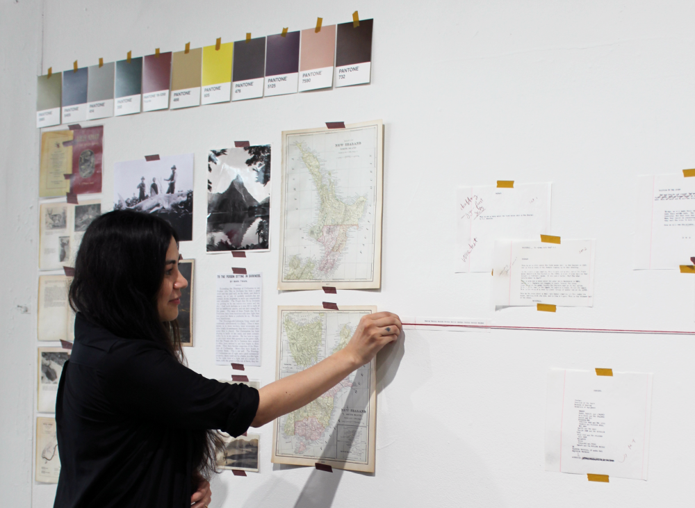 Hussey pinning the red timeline string to the gallery wall, surrounded by papers, maps, images and color swatches.