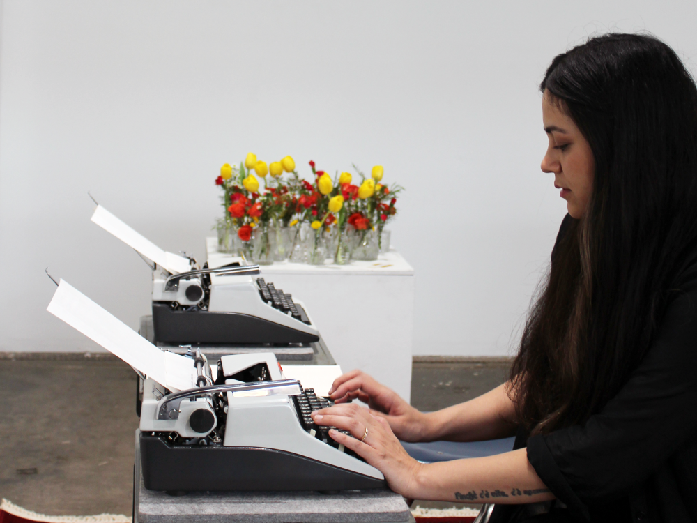Hussey types on one of her typewriters, with the other one in the background. Flower vases can also be seen in the background.