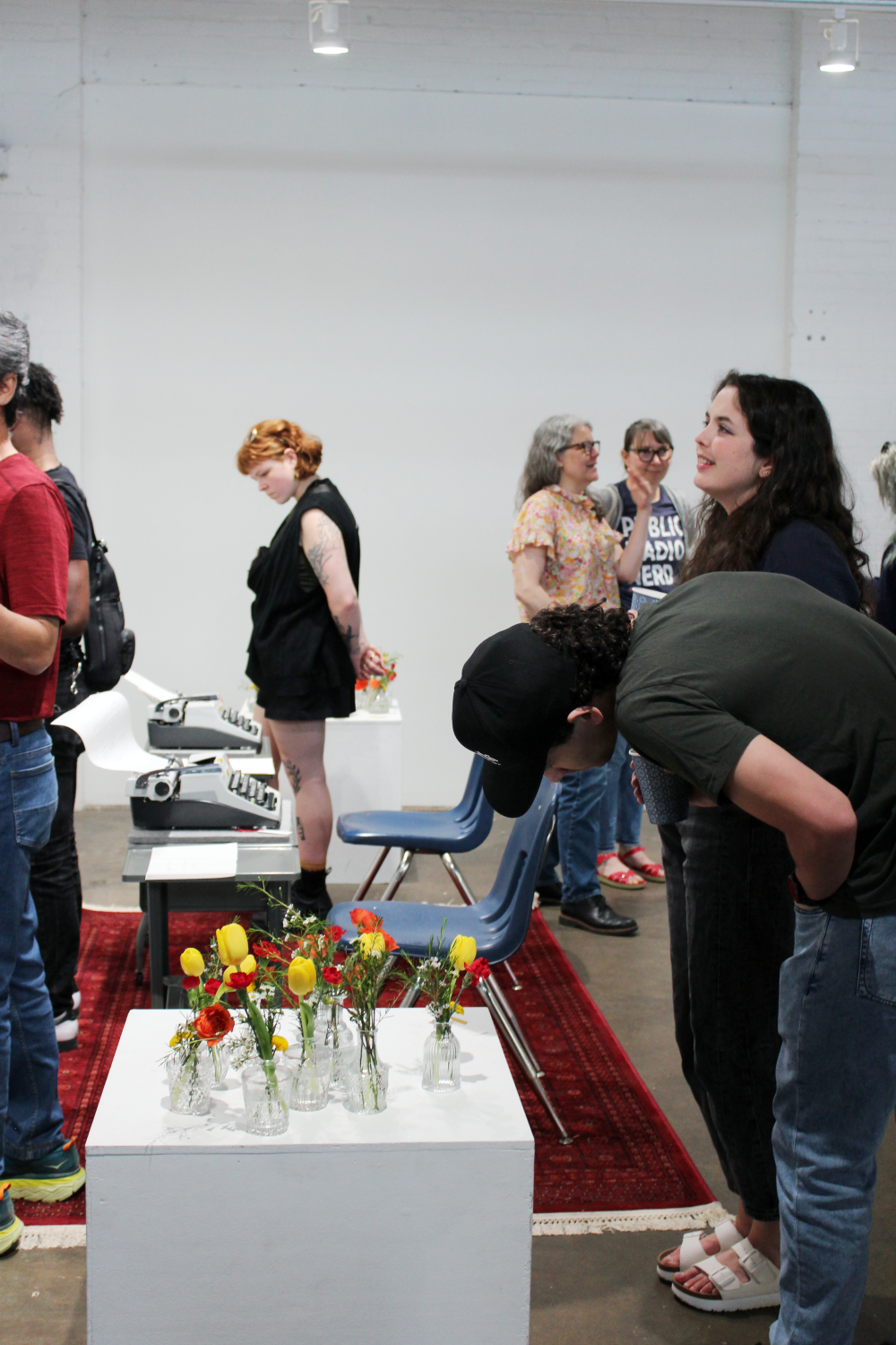 Attendees gathered in the gallery space. One is bending down to look at the flower vases.