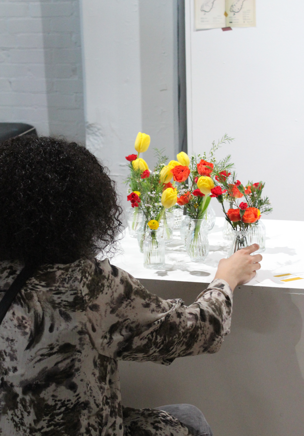 The back of a woman as she picks up a flower vase.