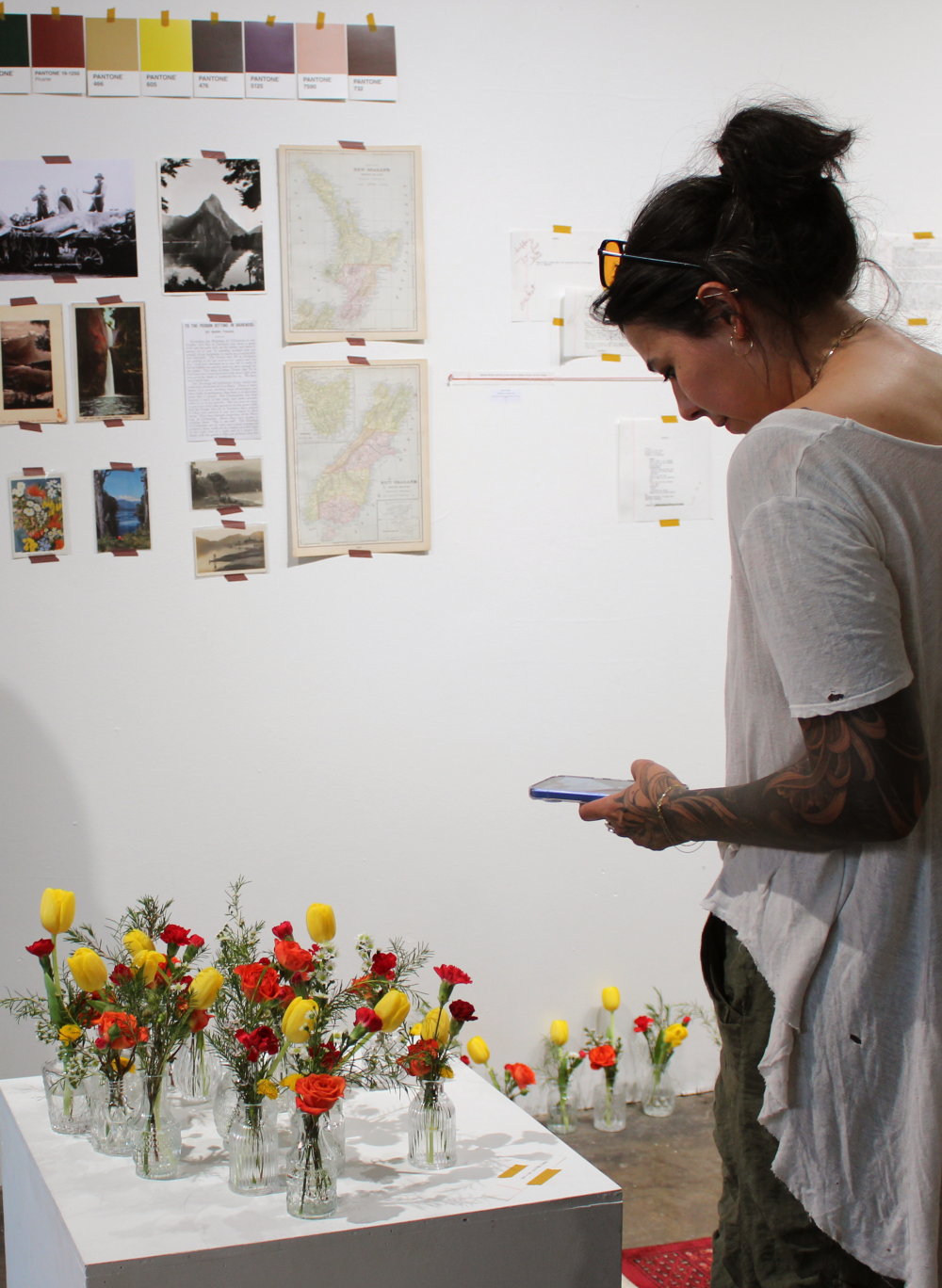 A woman takes a photo of the flower vases on display. The gallery wall can be seen in the background.