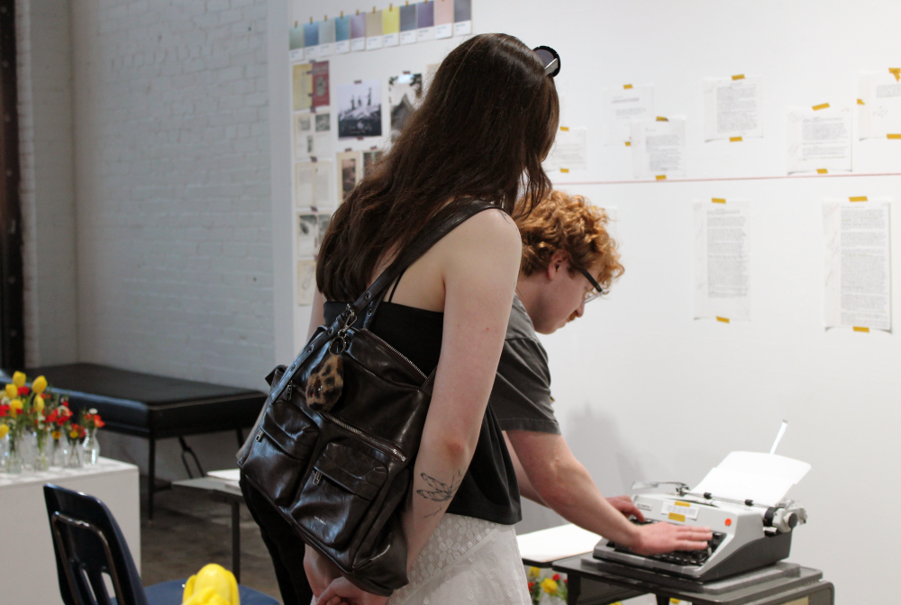 Washburn types on the typewriter while a woman watches over his shoulder. 