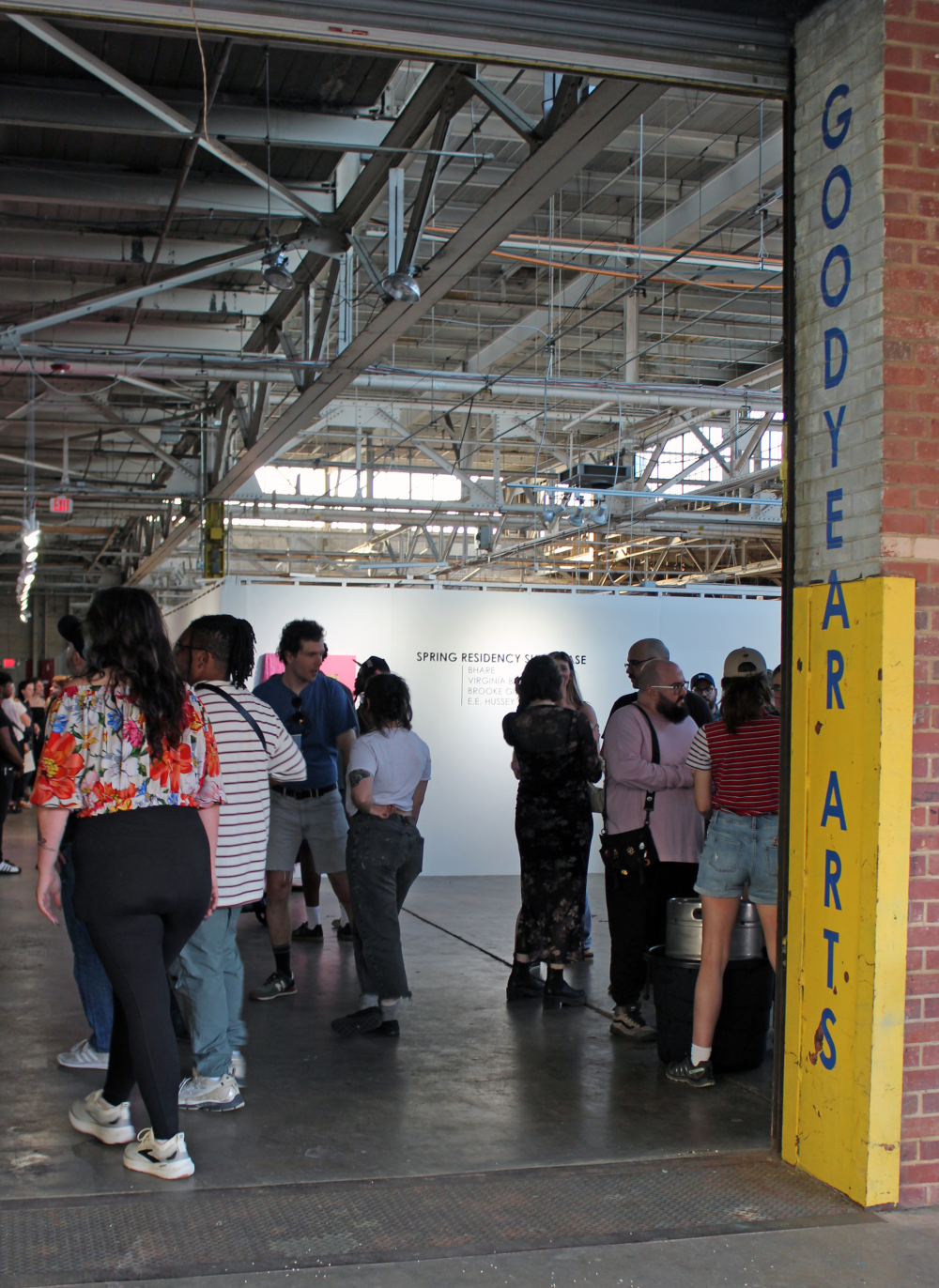 Looking into the Goodyear Arts space, with people standing and talking and a "Spring Residency Showcase" sign on a wall in the background. 