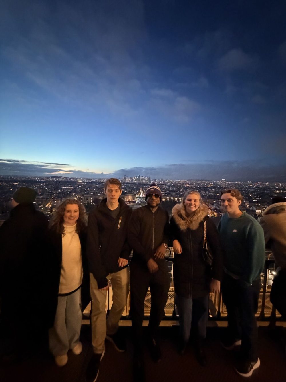 Watson poses with the students on a high viewpoint at night, with a view of Paris in the background.