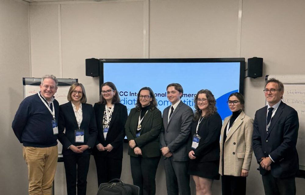 The team poses for a photo with other participants in front of a presentation screen that reads, "ICC International Commercial Mediation Competition".