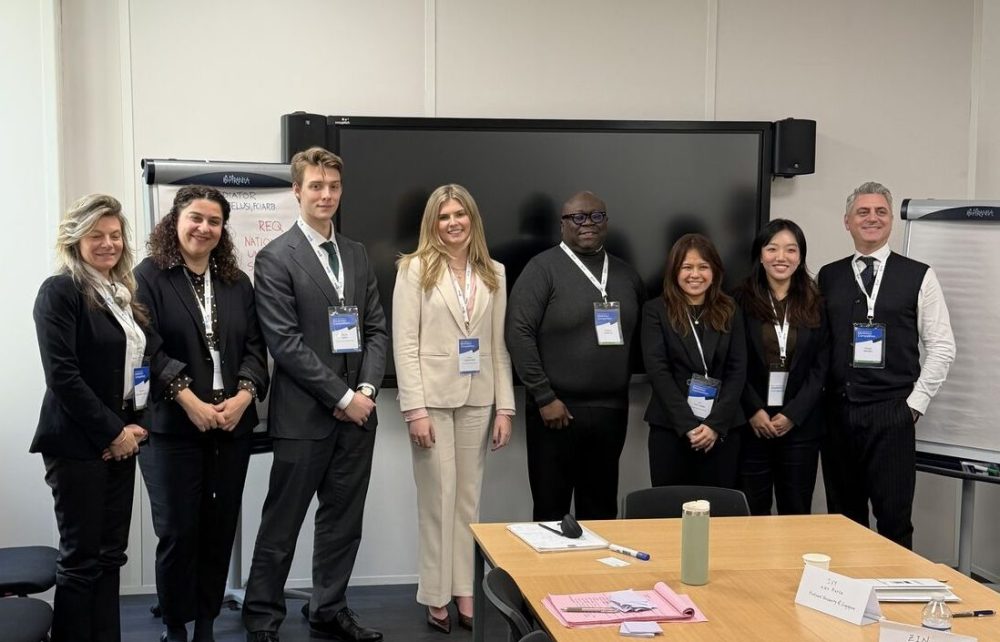 The team poses for a photo with other participants in a room with a table and presentation screen in the background.