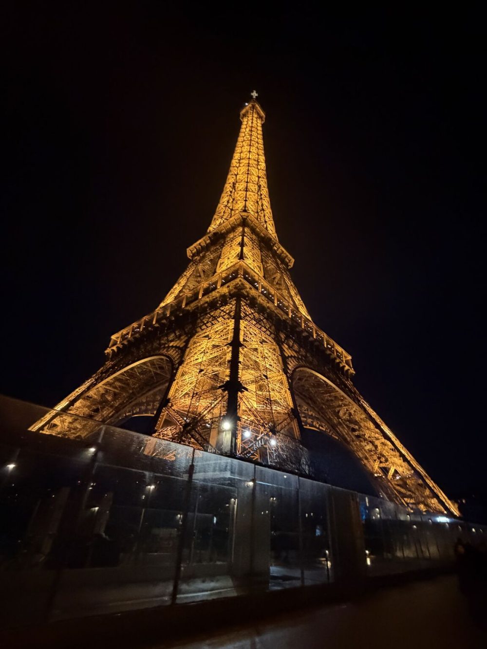 Looking up at the Eiffel Tower at night. It is lit up with yellow lights. 