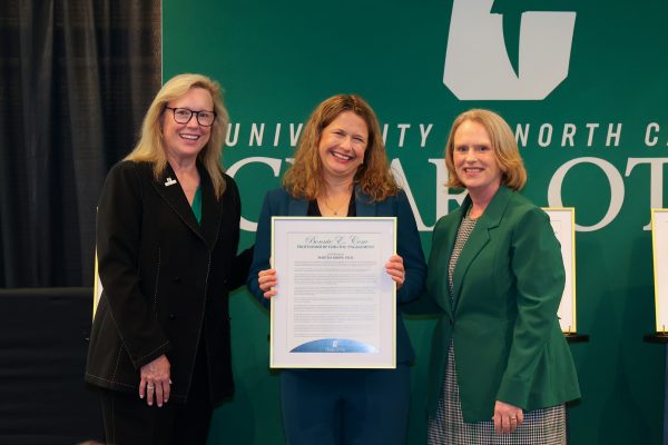 Chancellor Sharon L. Gaber and Provost Jennifer Troyer stand smiling with awardee Martha Kropf, who holds a large framed award.