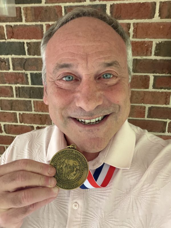 Steven G. Rogelberg, chancellor’s professor at UNC Charlotte, wears the 2026 North Carolina Governor’s Medallion Award for Volunteer Service around his neck, holding up the medal and smiling for the camera.