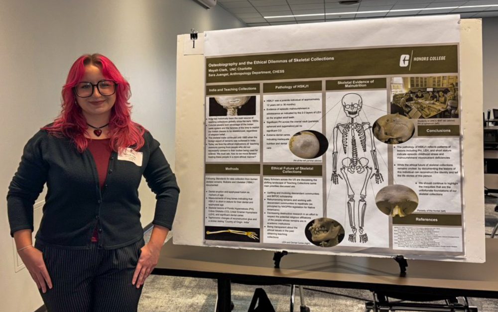 Mayah Clark, UNC Charlotte anthropology student in the College of Humanities & Earth and Social Sciences who conducted undergraduate and honors research, stands with a poster of her research during the UNC Charlotte Honors College research conference in fall 2025.