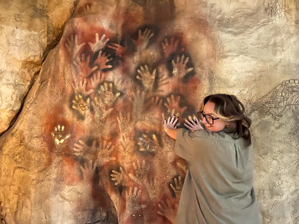 Mayah Clark, UNC Charlotte anthropology student in the College of Humanities & Earth and Social Sciences who conducted undergraduate and honors research, places her hands over handprints at the Smithsonian Museum of Natural History and smiles over her shoulder.