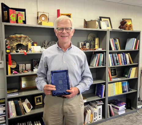 Jean-Claude Thill, UNC Charlotte Knight Distinguished Professor in the CHESS Department of Earth, Environment and Geographical Sciences, stands in front of bookcases holding the Carolyn Merry Mentoring Award.