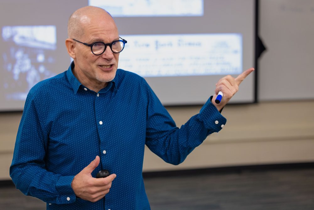 Oscar Lansen, UNC Charlotte Teaching Professor in the Department of History in the College of Humanities & Earth and Social Sciences, speaks to his class and gestures with his hands.