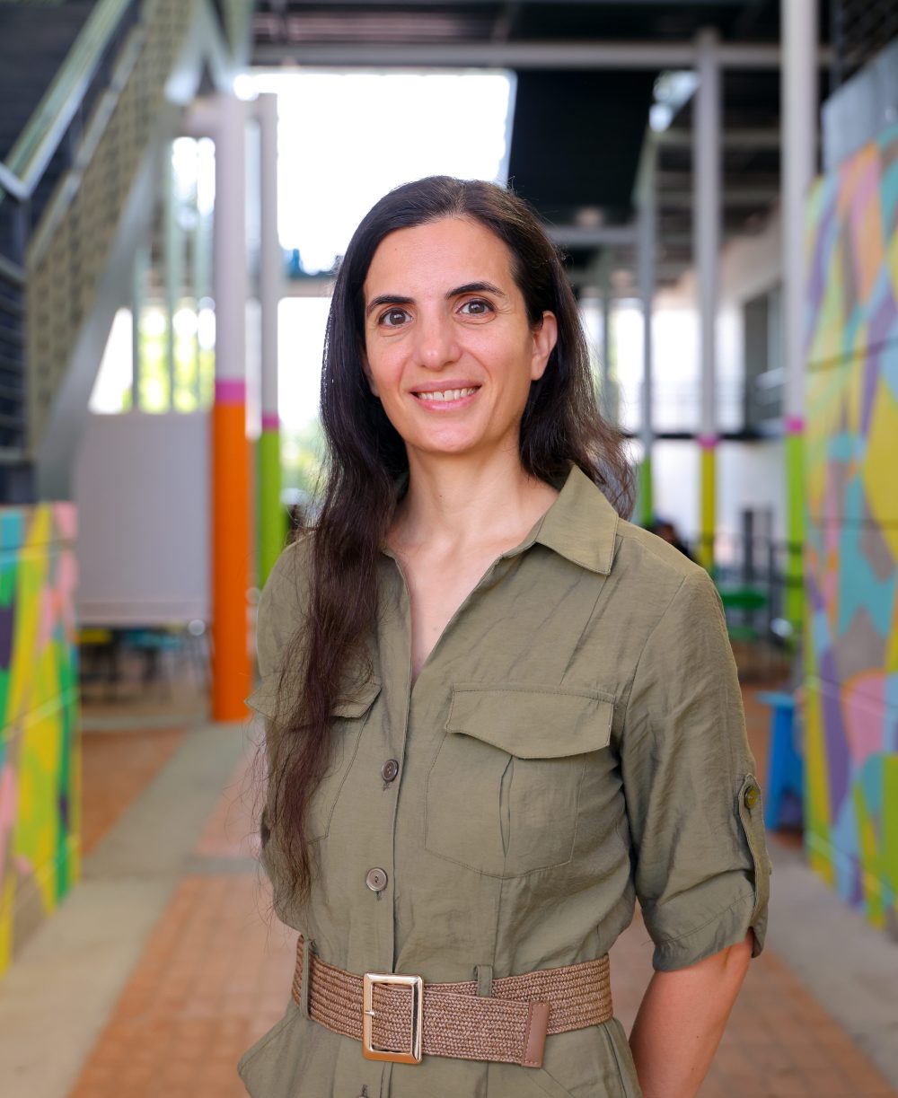 Alexia Galati, Ph.D, associate professor of psychological science and director of the Cognitive Science program, wears a green dress and smiles in an outdoor hallway on UNC Charlotte's campus.