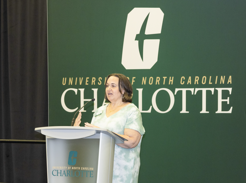 Shannon Homesley speaks at a UNC Charlotte podium in front of a Niner green background with the University of North Carolina at Charlotte logo during the 2026 ACE Alumni awards.