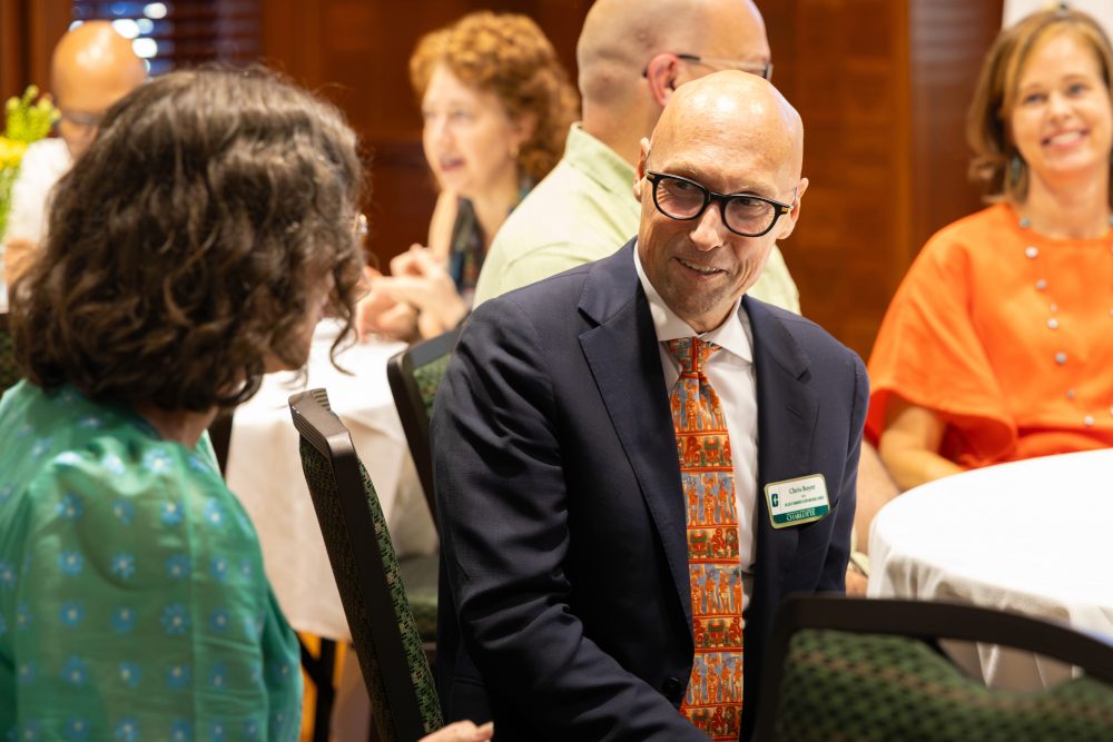 CHESS Dean Chris Boyer wears a suit and patterned tie smiling while conversing with UNC Charlotte Writing Resource Center Director Katie Garahan at the Harris Alumni Center during the 50th anniversary celebration for the UNC Charlotte Writing Resource Center.